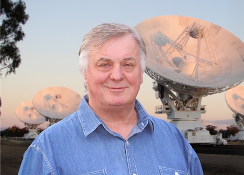 Man in a blue shirt stands in from of a radio telescope array