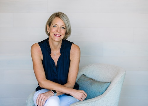 Kirsten sits on a blue chair against a white wall