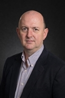 Headshot of Dr Hartley in front of a black wall