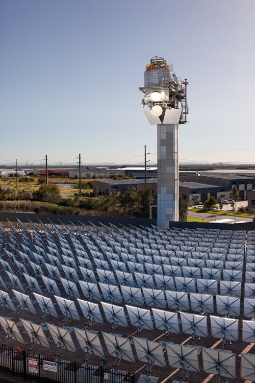 A tall tower stands behind a field of solar panels