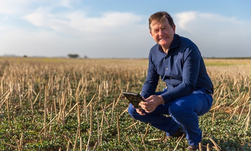 Anthony Willmott crouched in a paddock using the Rural Intelligence Platform on a tablet. 
