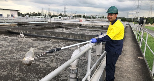 Scientist in hard hat and high visibility vest stands beside wastewater pond
