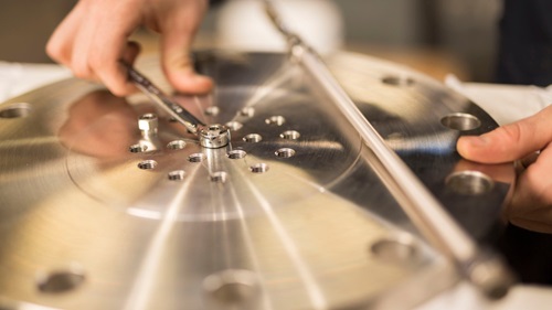 Hands use a spanner on a steel disc