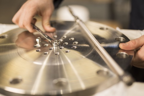 Hands hold a spanner above a steel disc.