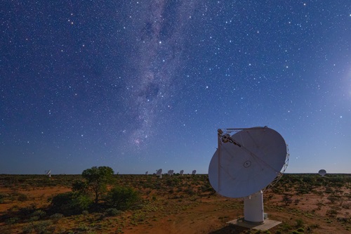 Close up of one of the ASKAP telescopes in the foreground shown during the night with several others in the distance. 