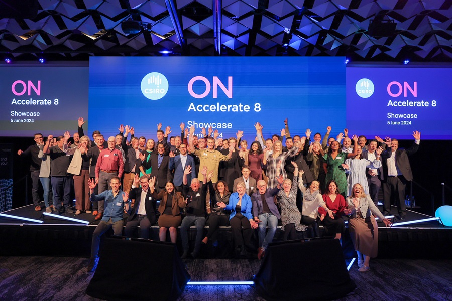 a group of people are standing on stage, in front of screens that say 'ON Accelerate 8 Showcase', with their hands in the air and smiling