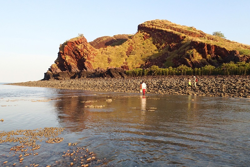 People wade through shallow water infront of a rocky mound
