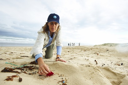 Researcher kneeling on beach  picking up a piece of marine debris