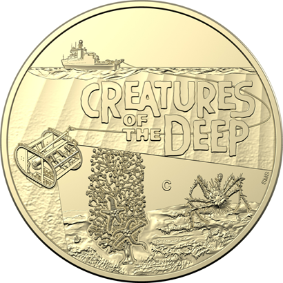A round gold coin with a picture of a ship, coral, crab, camera and the words 'Creatures of the Deep'.