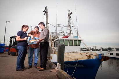 Researchers and industry inspect a prawn catch with a fishery boat in the background