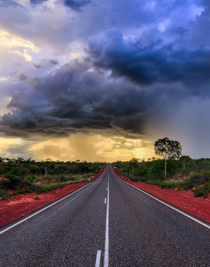 Empty road stretching to the horizon with grey clouds looming overhead.