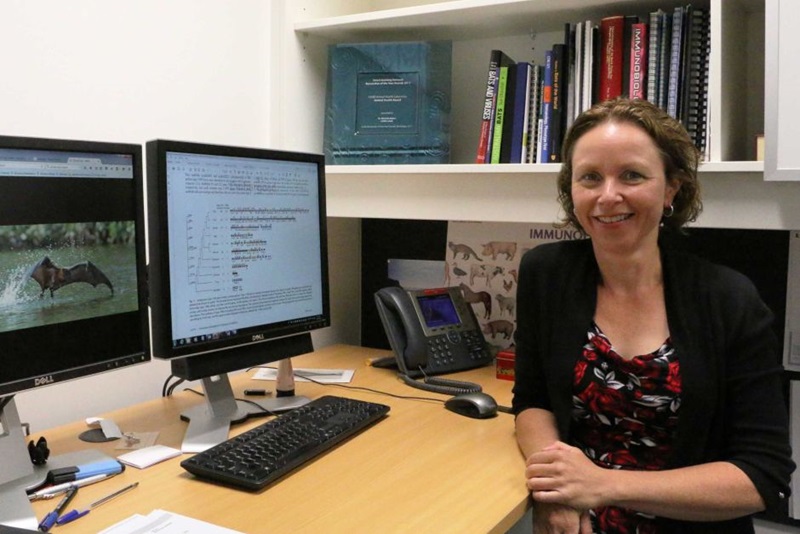 A woman sitting at her desk with two computer screens in the background.