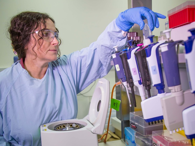 A woman in a blue lab coat working at a lab bench.