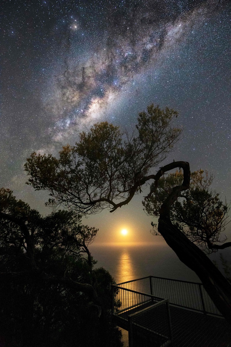 Moon rising over a body of water with the milky way above