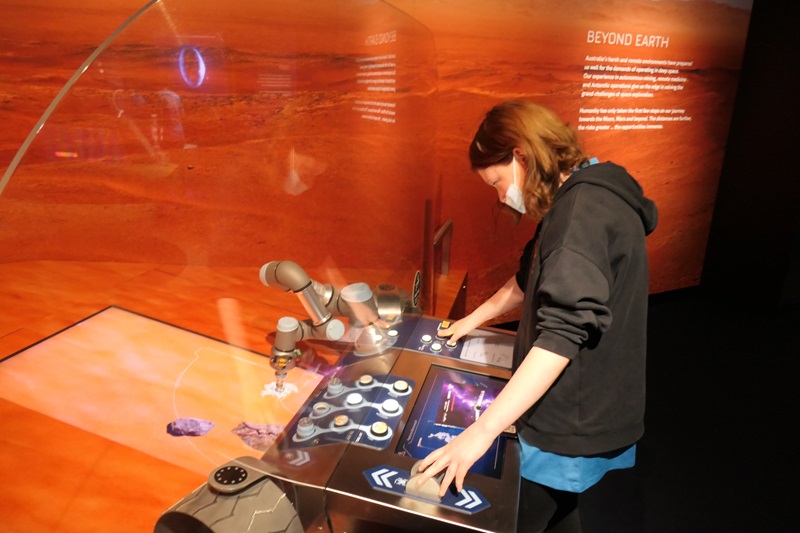 Dana is leaning over the control panel of an Australian Space Agency exhibition exploring life on Mars and beyond.