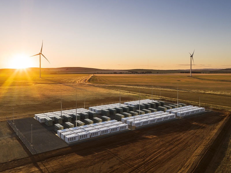 Sunset or sunrise shot of a large paddock containing wind turbines and industrial scale batteries. 