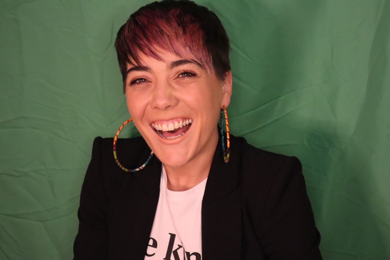 a young woman wearing a black blazer and large earrings smiling into the camera. 