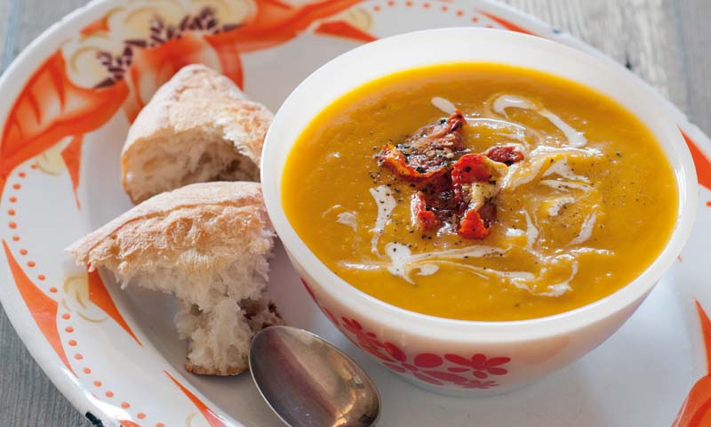 Bowl of pumpkin soup with two chunks of bread beside it. 