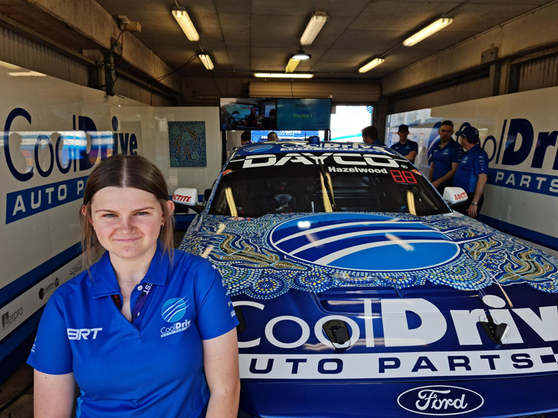 Young Indigenous woman stands in front of a painted racecar.