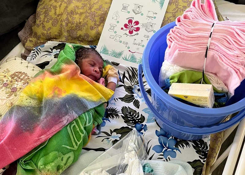 A newborn baby lying next to a bundle of reusable nappies and other items donated by Mamma's Laef. 