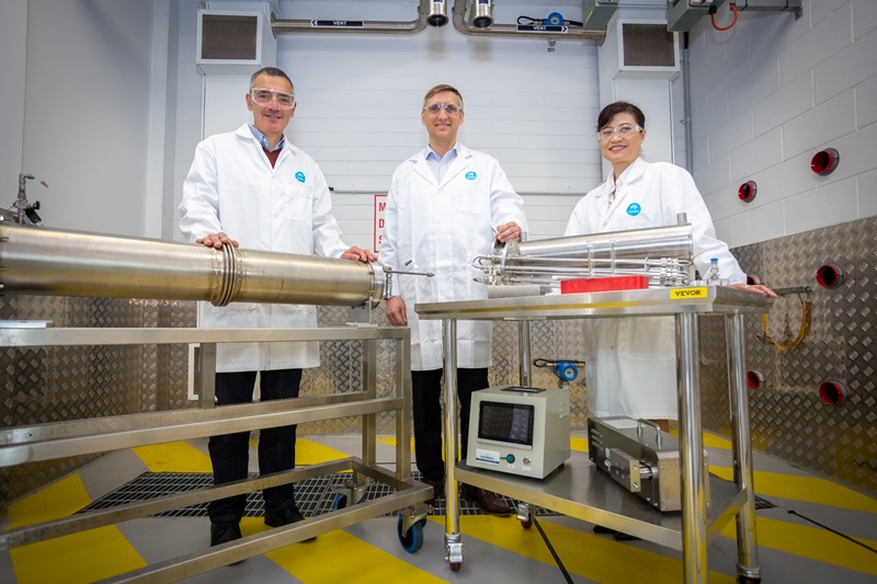 Three people in labcoats standing behind shiny industrial equipment