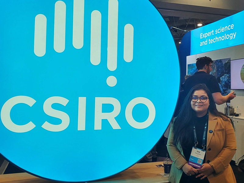 Isis standing next to a large light up CSIRO logo smiling at the camera