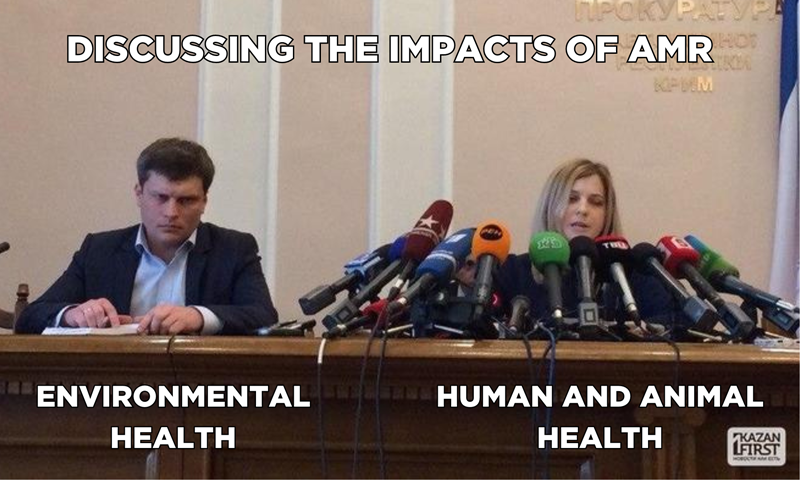 Two speakers sit beside each other representing the discussions of AMR. The first represents environmental health, and has no microphones. Next to them sits 'Human and animal health' with a whole bank of microphones in front of them.