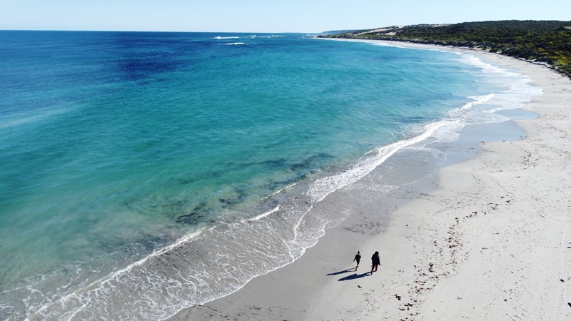 Two people walk along a beach