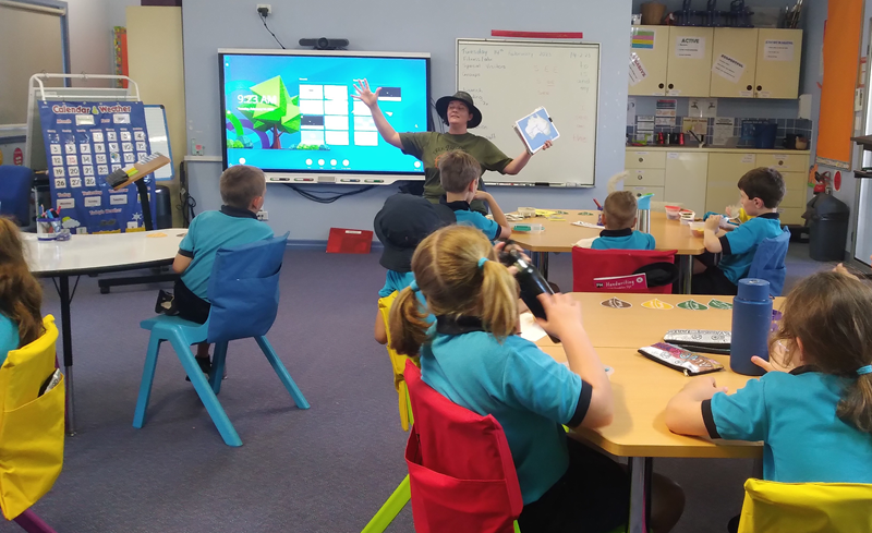 Lizz Hills, teacher stands in a classroom of seated primary school children