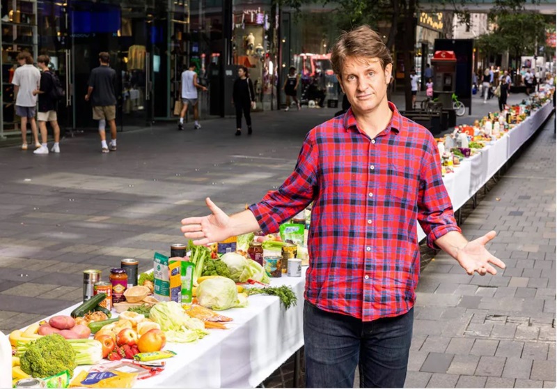 Craig Reucassel stands alongside a 50m long table covered in food, which is the amount one family wastes in a year.