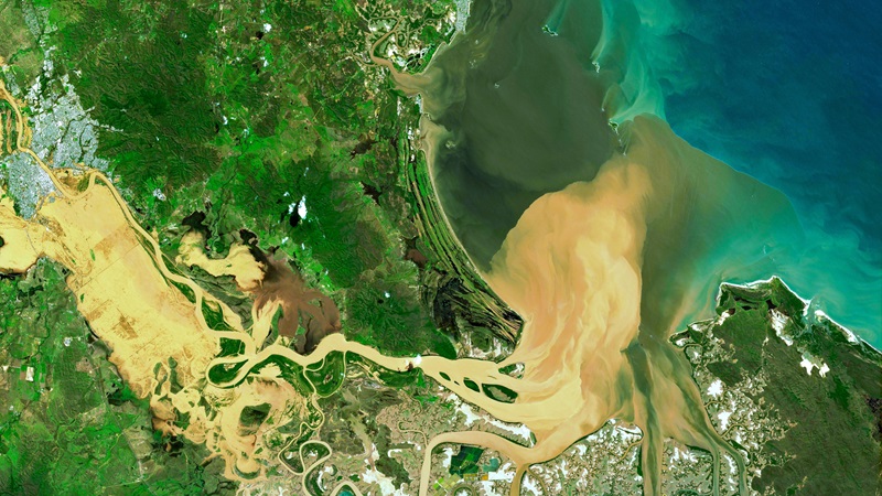 Satellite image showing a light brown sediment plume and a dark grey-brown dissolved carbon plume flowing from the flooded Fitzroy River Fitzroy River out to Keppel Bay in QLD.