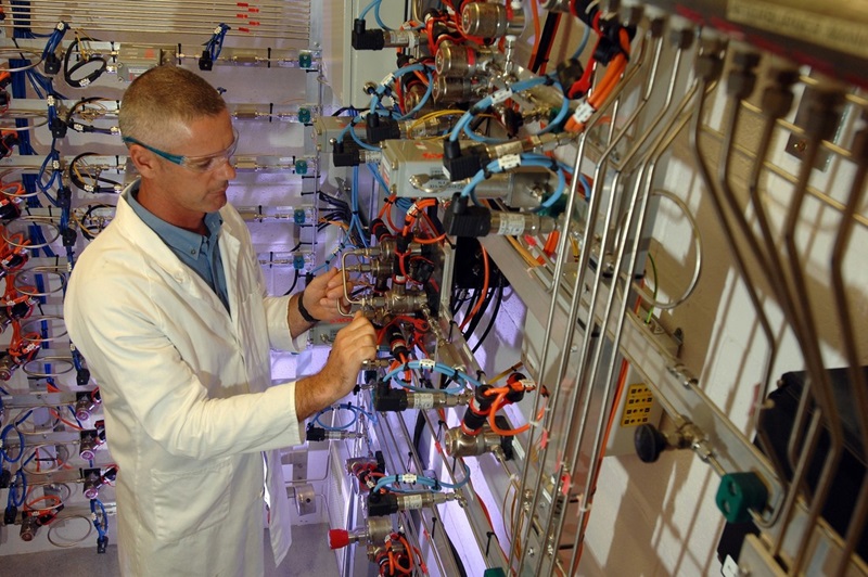 A man in a labcoat and protective goggles handles complex wiring in a lab. 