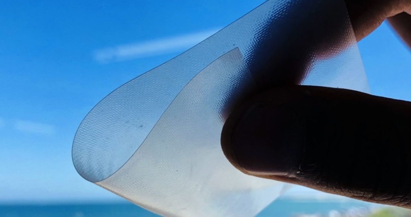 A thin, nearly transparent piece of film is folded between two fingers. 