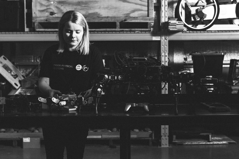 A black and white photo of Rosie Attwell looking down at a robot thoughtfully 