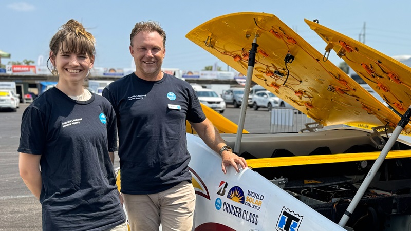 Two people standing next to a solar powered vehicle.