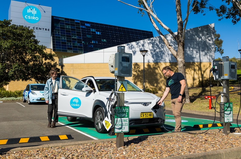 Two people charging an electric vehicle displaying a CSIRO logo outside a CSIRO building.