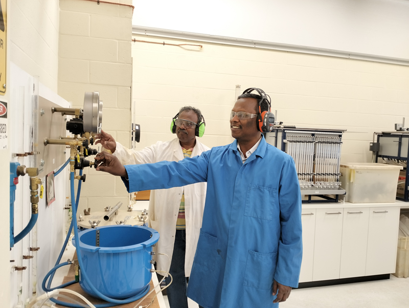 Two men in labcoats use some equipment at a lab. 