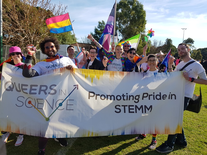  A group of happy, colourfully dressed people carry a banner promoting 'Pride in STEMM'