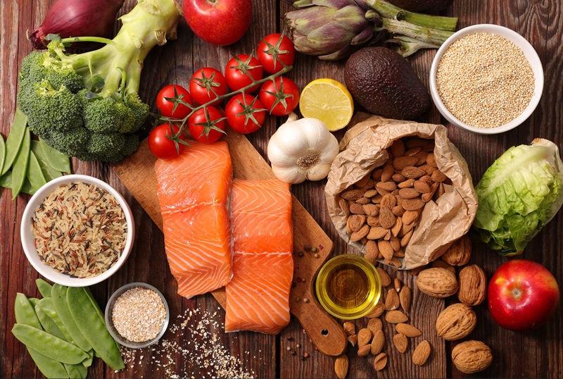 A range of vegetables, nuts and healthy proteins like salmon on a wooden countertop. 