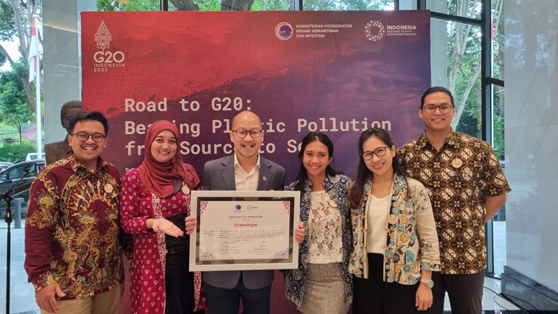 A group of men and women stand in front of a banner. They are holding a large framed certificate.