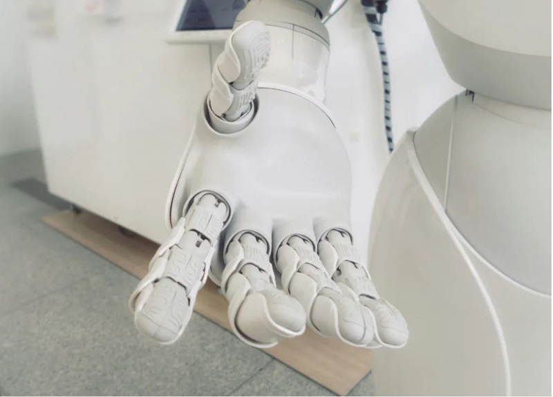 Close-up of robot hand.  It appears to be made of white plastic, and shows textural details on the fingers. 