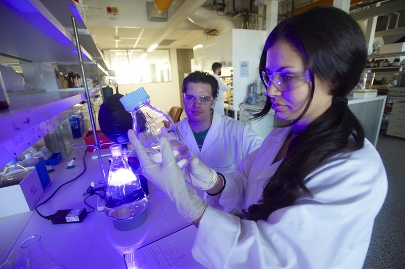 Two scientists looking at a jar containing a clear liquid in a lab environment