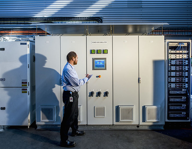 Researcher in front of a piece of machinery taking a reading and writing notes. 