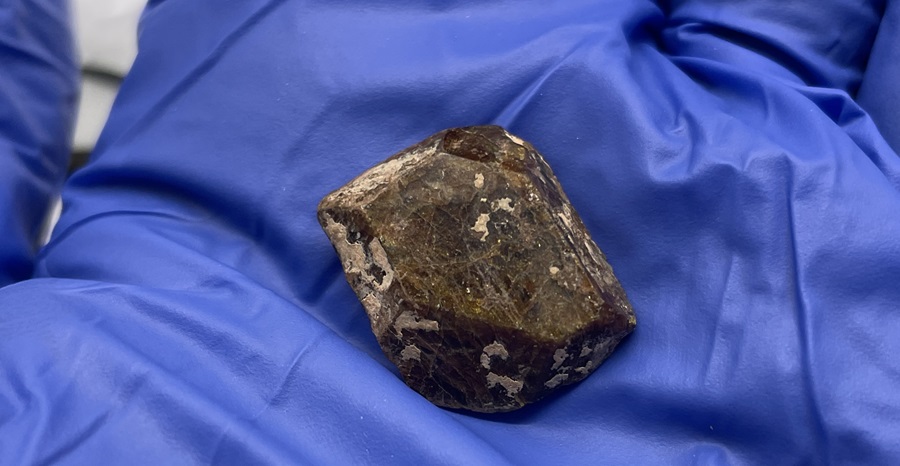 A small brown, roughly square rock sitting in the palm of a gloved hand