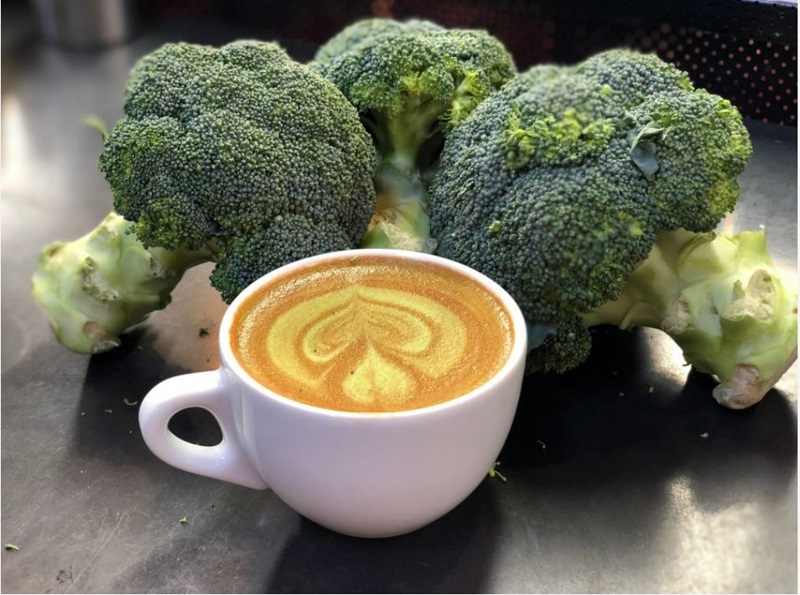 A cup of latte surrounded by pieces of broccoli