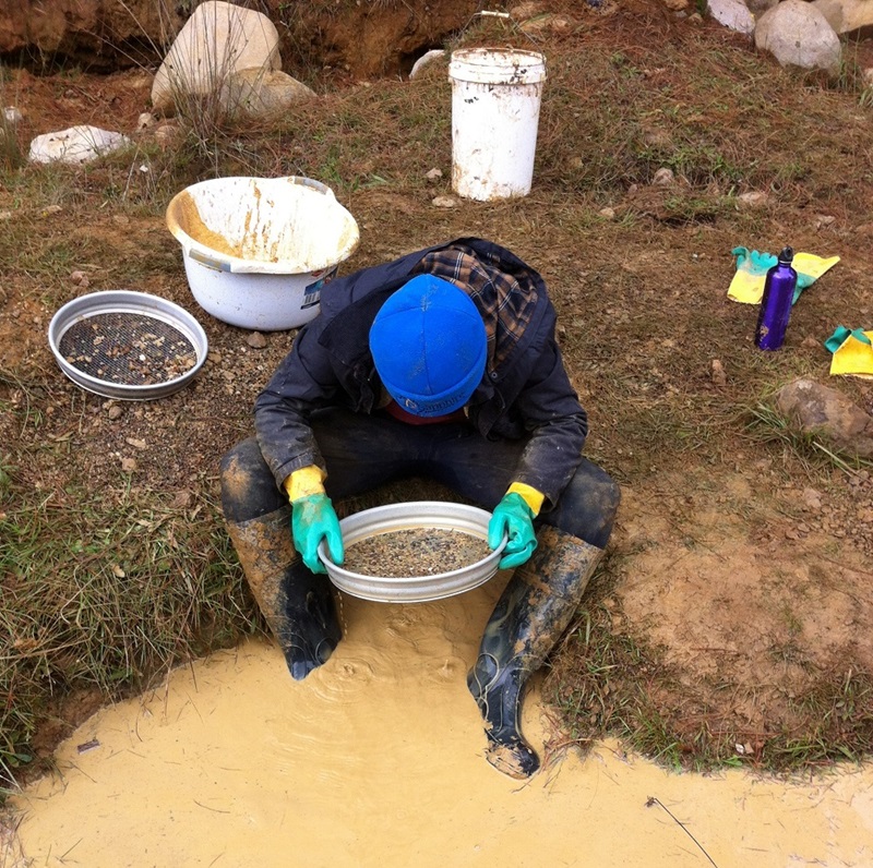 Man sitting in muddy water looking into sieve