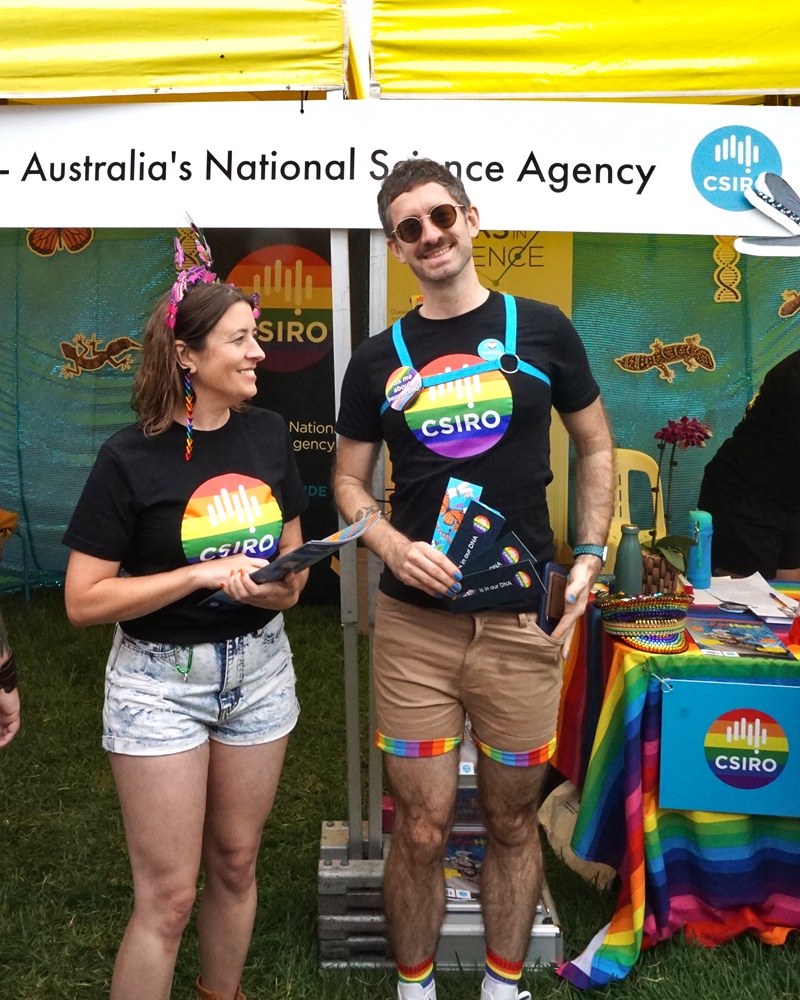 Two people in rainbow CSIRO logo shirts standing in front of a CSIRO-branded marquee at Midsumma 2024.