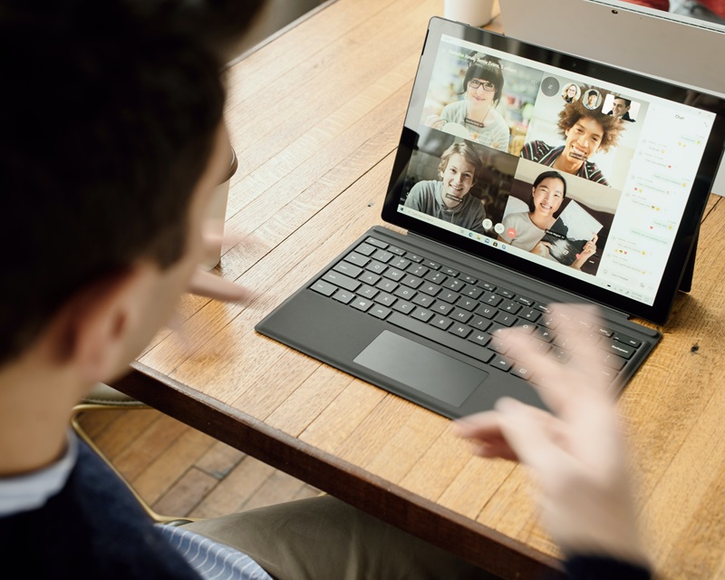 A shot from behind the shoulder of a person attending a virtual meeting with colleagues on a laptop. 