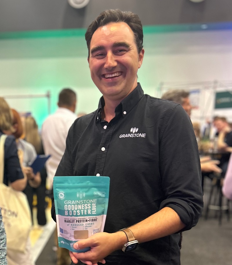 A man in a Grainstone shirt holds a packet of branded protein.