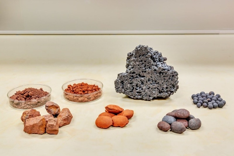 a selection of iron in various forms on a table, including iron ore, pig iron and iron pellets